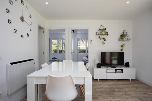 a white dining room with a white table and a tv at Apartament amb piscina i aparcament - Baixos amb jardinet in Calella de Palafrugell