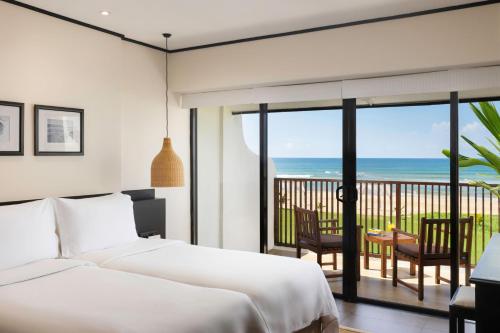 a bedroom with two beds and a balcony with the ocean at EKHO Surf Bentota in Bentota
