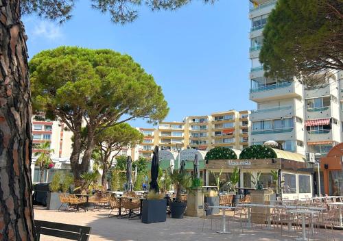 a park with tables and chairs and a building at Hôtel Le Carnon in Carnon-Plage