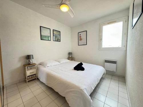 une chambre blanche avec un chat noir assis sur un lit dans l'établissement Valras-Loc - Appartement du stade, à Valras-Plage