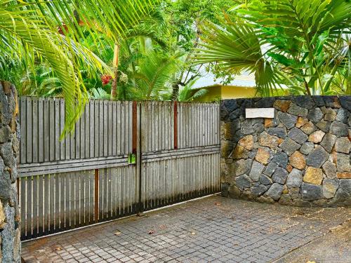 a fence and a stone wall with palm trees at Waka Lodge - House with garden in Blue Bay