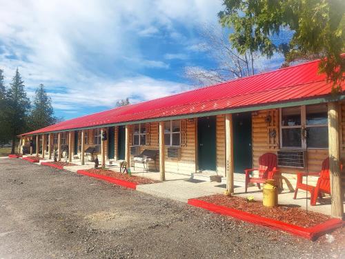 a wooden cabin with a red roof and red chairs at Moosewood Inn in Saint Ignace