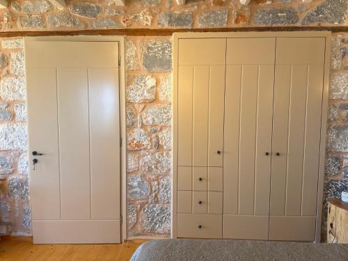 two white cabinets in a room with a stone wall at Pirgos Petropoulea in Poliána