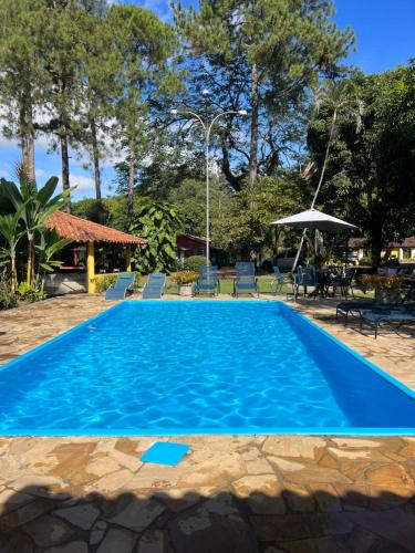 a blue swimming pool with chairs and an umbrella at Pousada Villa Luna in Penedo