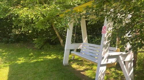 a white bench sitting in the grass under a tree at Pensiunea ANA Vistisoara in Vistisoara