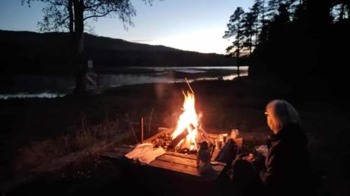 a woman sitting in front of a fire in a field at Fjällnära Villa i Vidsel in Vidsel