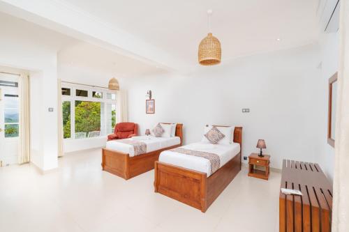 a white room with two beds and a chair at Rose Hill Bungalow in Gampola
