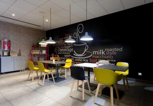 a restaurant with yellow chairs and tables and a black wall at B&B HOTEL Reims Centre Erlon in Reims