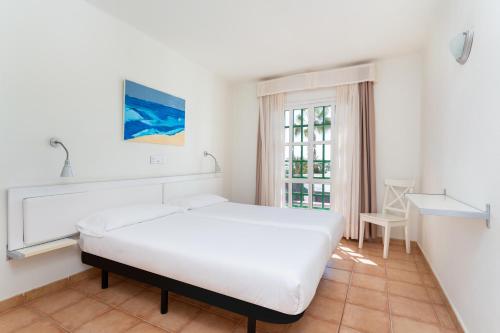 a white bedroom with a bed and a window at Apartamentos LIVVO Las Gaviotas in Puerto del Carmen