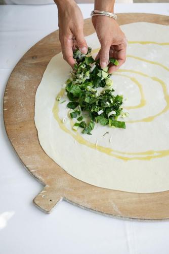 a person cutting greens on top of a pizza dough at Ikion Eco Boutique Hotel in Patitiri