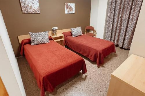 a room with two beds with red sheets and a chair at Hotel Anna in Cocentaina
