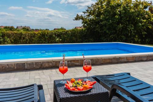 two wine glasses and a bowl of fruit on a table next to a pool at Kuća za odmor Dugo Selo M&A in Dugo Selo