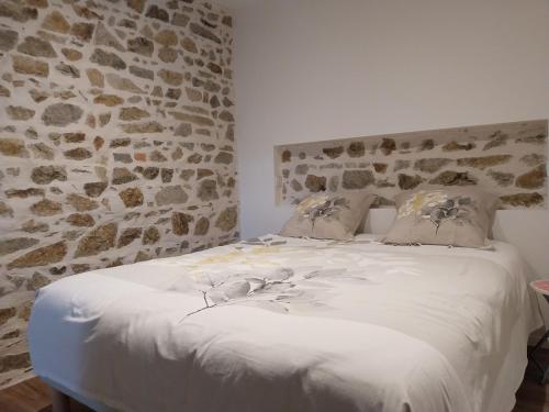 a bedroom with a white bed with a stone wall at La Petite Ferme Aux Prés in Saint-Germain-Lespinasse