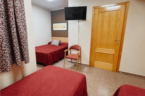 a room with two beds and a chair and a door at Hotel Anna in Cocentaina