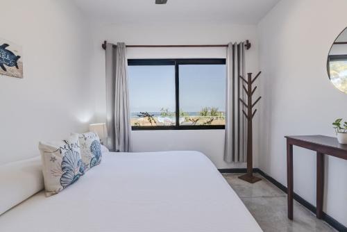 a white bedroom with a bed and a window at Vela's Condos Ocean Front in Puerto Morelos