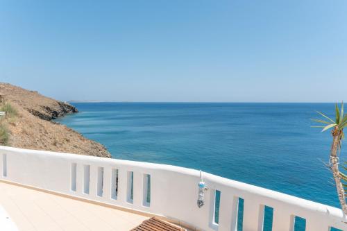 a white fence next to the ocean with a palm tree at Caldera Studios in Astypalaia Town