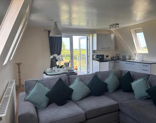a living room with a couch with pillows and a kitchen at Hayes Lodge Coach House in Chulmleigh