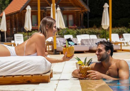 a man and woman sitting in a pool holding drinks at Wood Hills Hotel & Resort in Mayrūbā