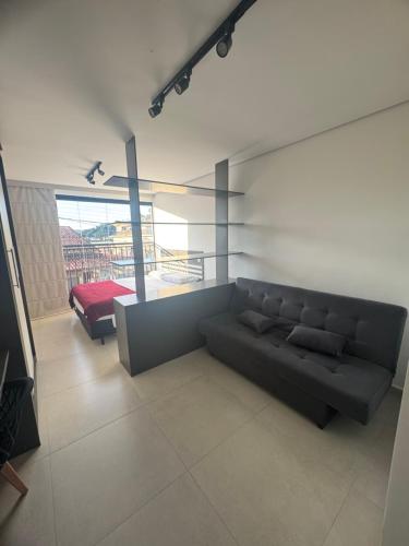 a living room with a black couch and a bed at Studio lindo com ar condicionado e piscina - Bela Vita - 104 in São Lourenço