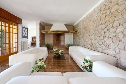 a living room with white couches and a stone wall at Villa Capinera, intera casa con parco privato in Punta Ala