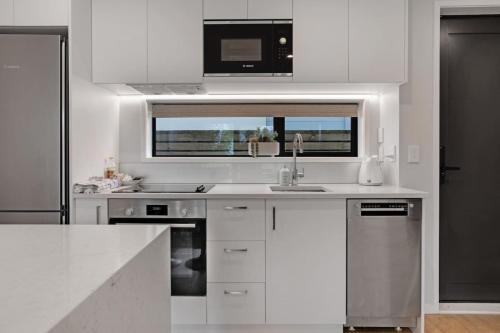 a white kitchen with a sink and a microwave at Modern Townhouse close to Airport and Hospital in Auckland
