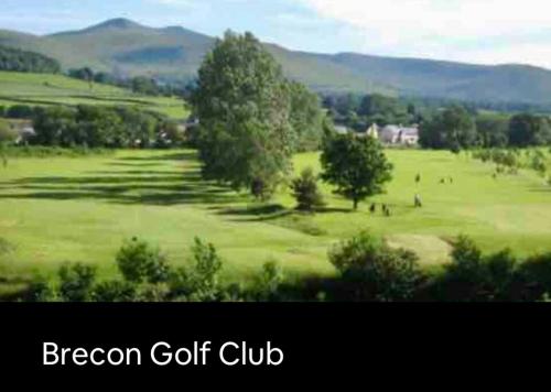 a green golf course with trees and mountains in the background at Kookaburra Cottage in Brecon