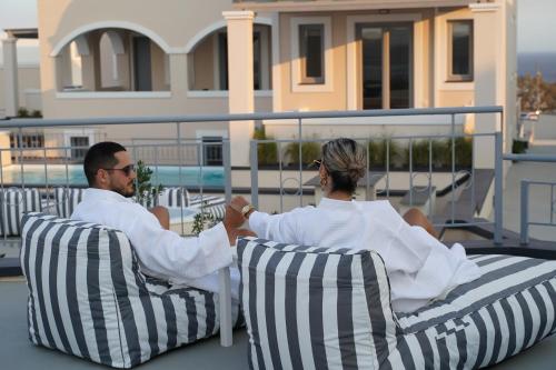 a man and a woman sitting in chairs on a balcony at The Noverian Bios Caldera Sunset Suites in Akrotiri