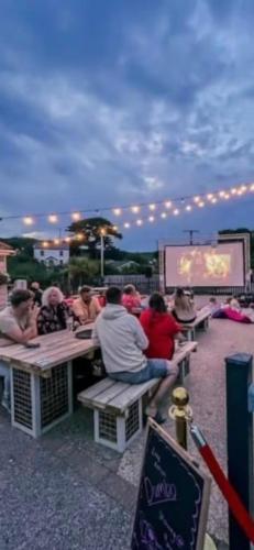un gruppo di persone sedute ai tavoli da picnic che guardano uno schermo di Newquay Bay Resort a Newquay