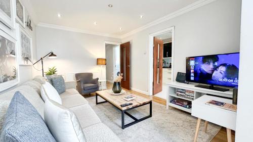a living room with a white couch and a tv at Lovely 4-Bedroom Kilburn Flat with Garden and Parking near Hampstead Heath, Abbey Road by Staylio London in London