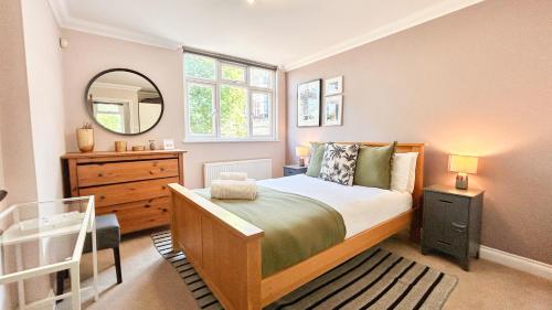 a bedroom with a bed and a dresser and a mirror at Lovely 4-Bedroom Kilburn Flat with Garden and Parking near Hampstead Heath, Abbey Road by Staylio London in London