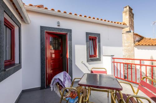a table and chairs on a balcony with a red door at Casa do Pisco - by Smarthomes in São Martinho do Porto