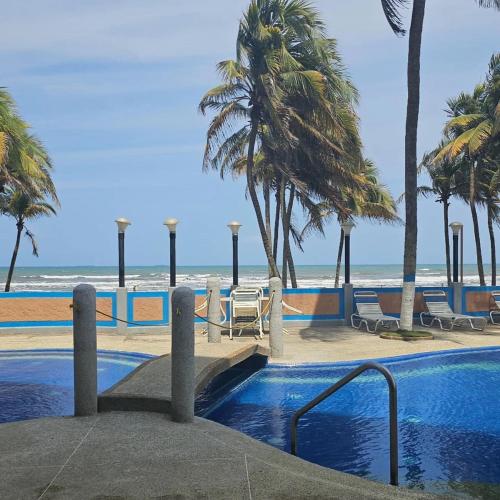 a swimming pool next to a beach with palm trees at Oceanfront apartment in Morrocoy, Tucacas, PB in Tucacas