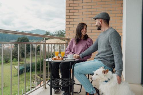 a man and woman sitting at a table on a balcony with a dog at Bed & Breakfast EQUITARE RURAL in Miranda do Corvo