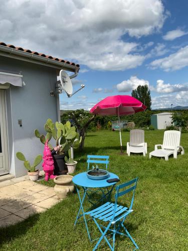 eine Terrasse mit Tisch und Stühlen und einem rosa Sonnenschirm in der Unterkunft Studio la maison bleue in Issoire