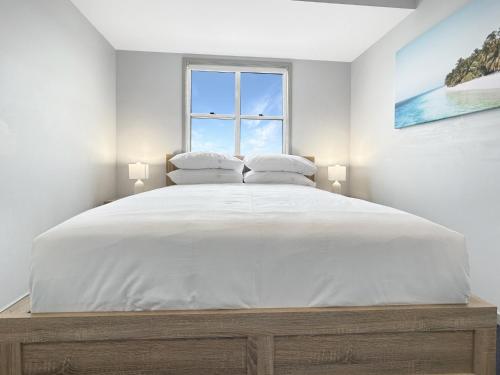 a white bedroom with a large bed with a window at 3-Bed with Alfresco Dining & Pool in Batemans Bay in Batemans Bay