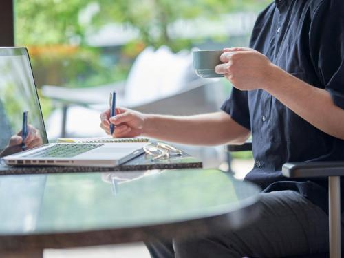 a man sitting at a table with a laptop and a cup of coffee at CROSS Life Hakata Tenjin in Fukuoka