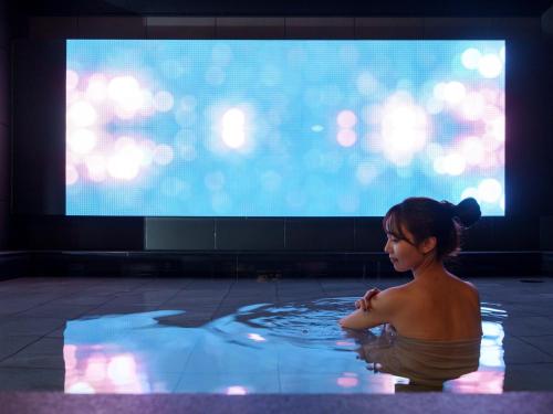 a woman in a bathtub in front of a television at CROSS Life Hakata Tenjin in Fukuoka