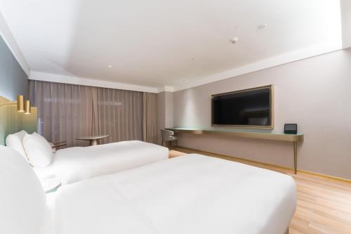 two beds in a hotel room with a flat screen tv at Manxin Hotel Guangzhou Baiyun Airport Branch in Guangzhou