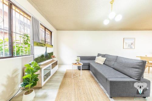 a living room with a gray couch and windows at KozyGuru | Cabramatta | Spacious 3BR Townhouse in Cabramatta