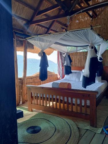 a bedroom with a canopy bed with a view of the ocean at Quest at Cape Maclear in Chembe