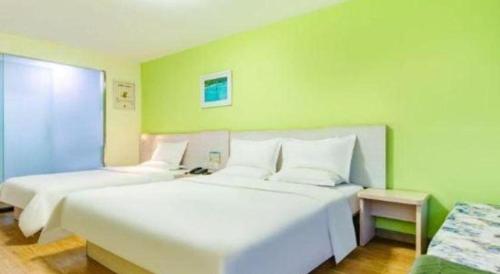 two white beds in a room with green walls at 7 Days Inn Tianjin Development Zone 3rd Street Wanli in Binhai