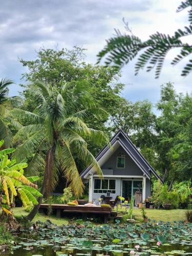 a house with a palm tree in front of a pond at บ้านสวนปรีดา-Preda Garden Home in Sam Phran