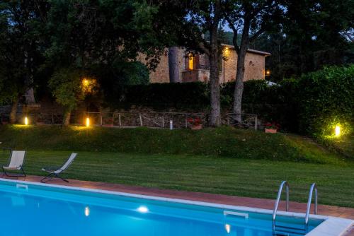 a swimming pool with two chairs and a house at night at TORRE DI PACIANO 10&2, Emma Villas in Paciano