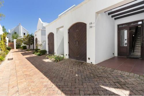 a white house with a brown door and a brick sidewalk at Winelands Golf Lodges 18 in Stellenbosch