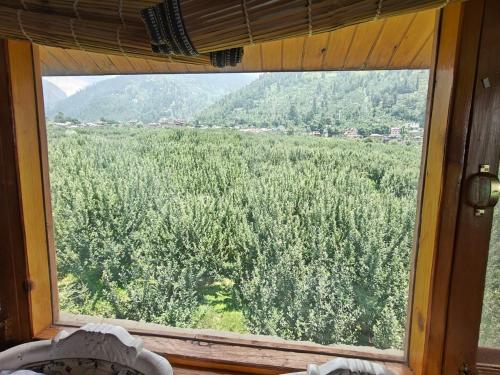 a window with a view of a field of trees at Apple Garden Cottage in Manāli