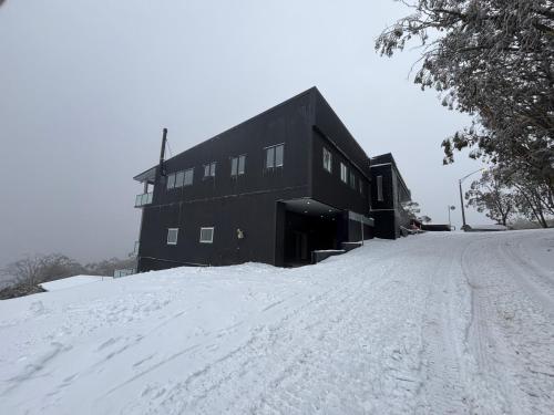 a black building on top of a snow covered road at Cooroona Alpine Lodge in Falls Creek