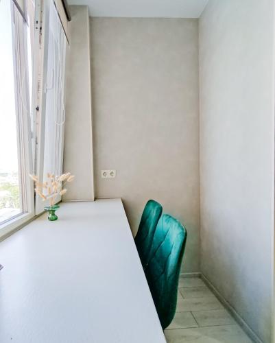 a table and a green chair in a room with a window at Радужная студия Вокзал Харьков-Пассажирский in Kharkiv