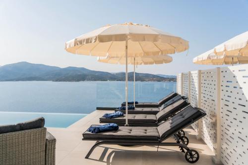 two lounge chairs with umbrellas on a balcony at Alexandria Seaside Luxury Villas in Kriaritsi in Sikia