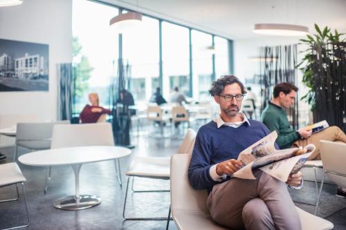 a man sitting in a chair reading a newspaper at Seminarhotel CAMPUS SURSEE in Sursee