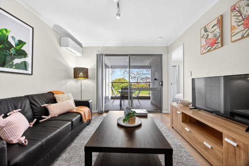 a living room with a black leather couch and a television at Coastal Comfort in Rockingham 2BR Apartment with Parking & Balcony in Rockingham